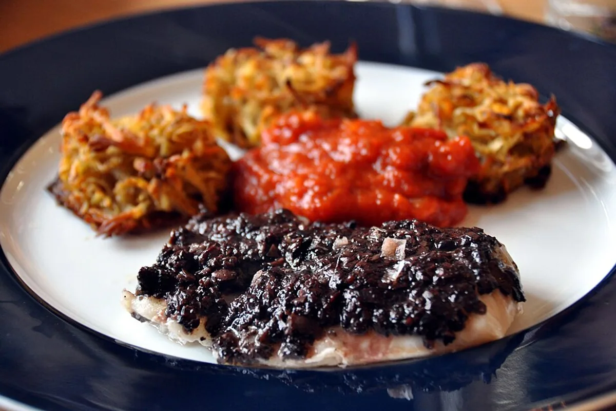 Baked cod under black olive tapenade with tomato sauce and crisp rosti