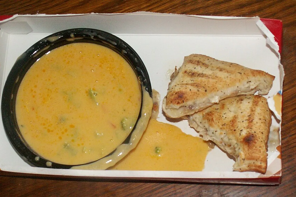 Bowl of broccoli cheddar soup with two toasted cheese sandwich halves