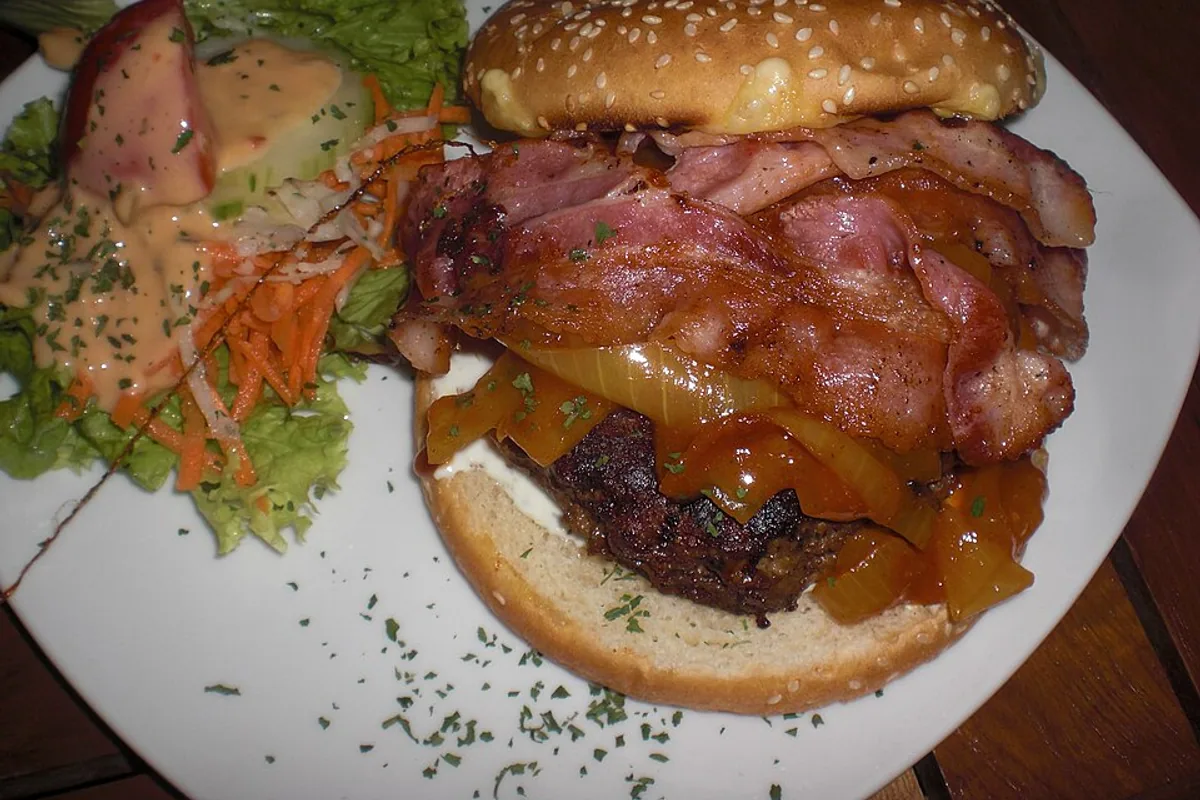 Bacon cheeseburger with melted cheese sauteed onions and a dressed side salad