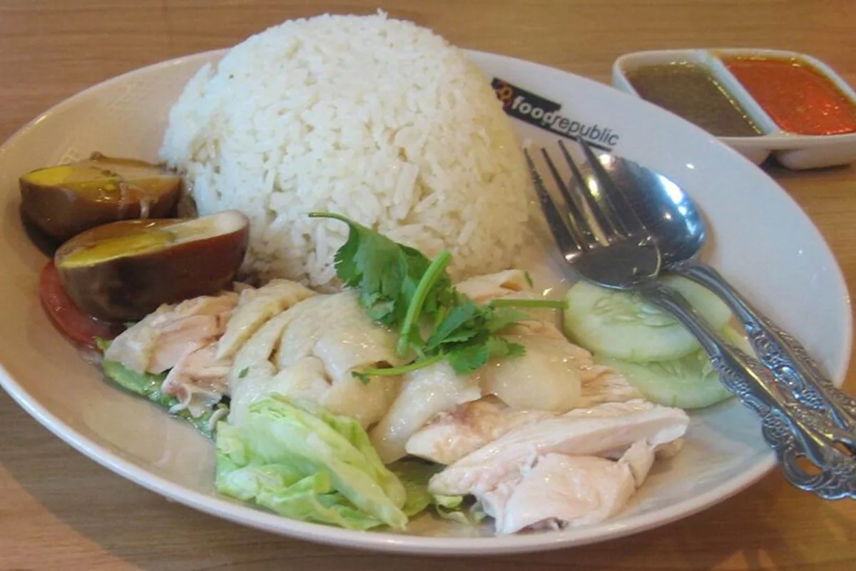 Hainanese chicken rice plate with sliced poached chicken cucumber cabbage cilantro and sauces