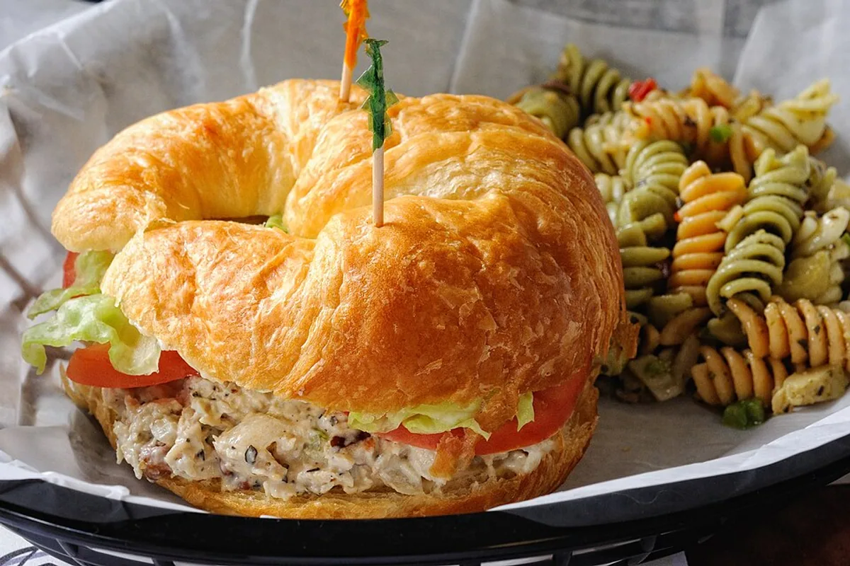 Chicken salad croissant with lettuce beside tri-color pasta salad
